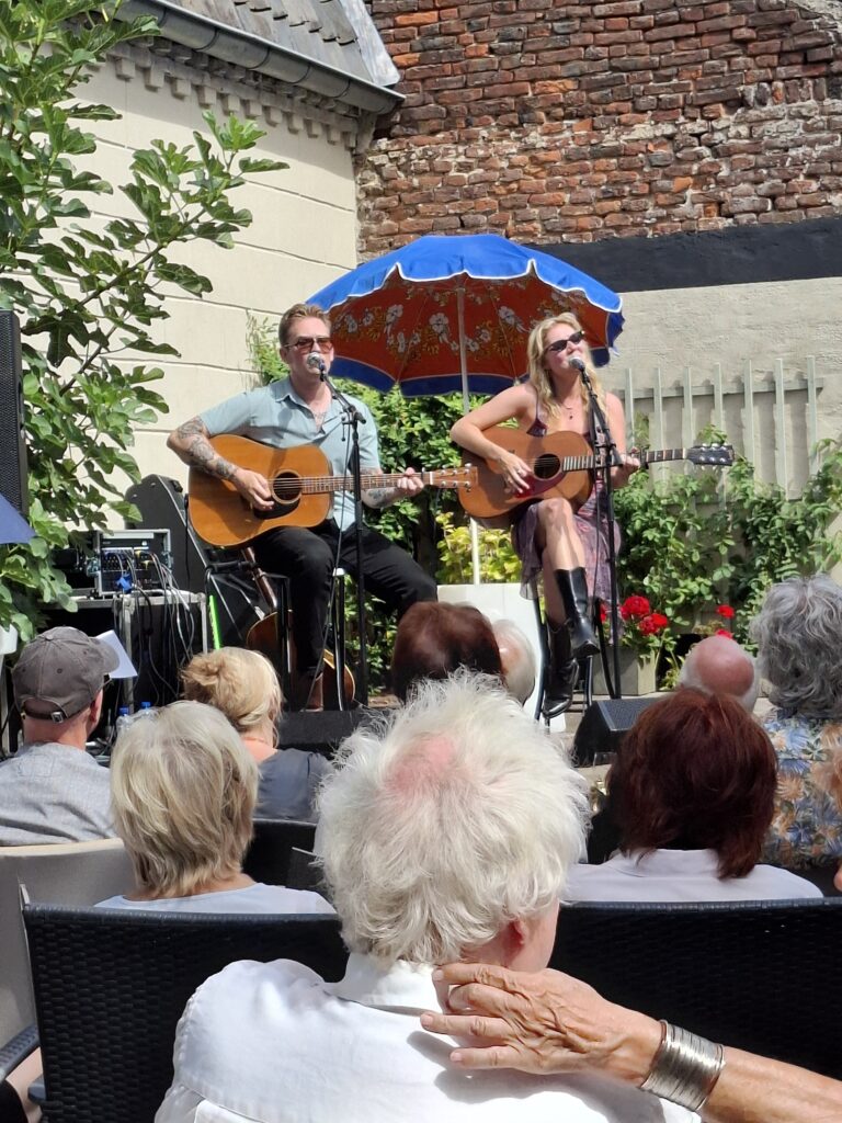 Zangeres Jana Mila treedt op met gitaar tijdens een intiem, zonnig tuinconcert in Thorn.